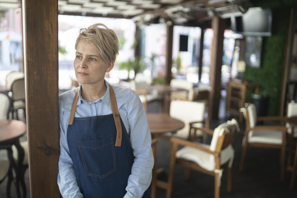 Female restaurant owner standing in the middle of her empty restaurant 