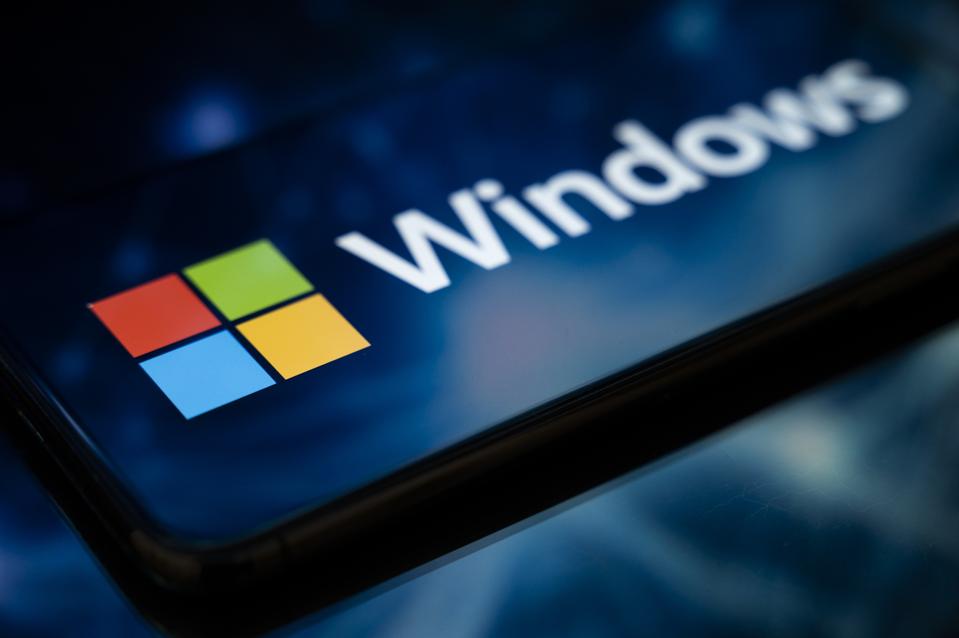 The Windows logo appears on the screen of a smartphone reflecting an abstract illustration in blue colors. 