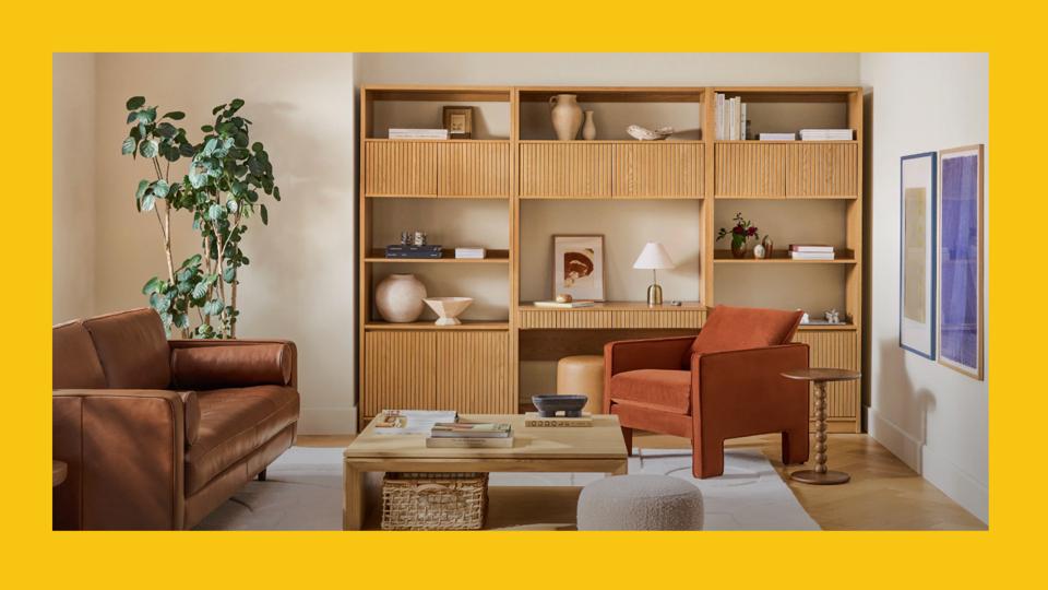 Lifestyle photo of a living room with a brown couch, wood book shelves and a dark orange chair.