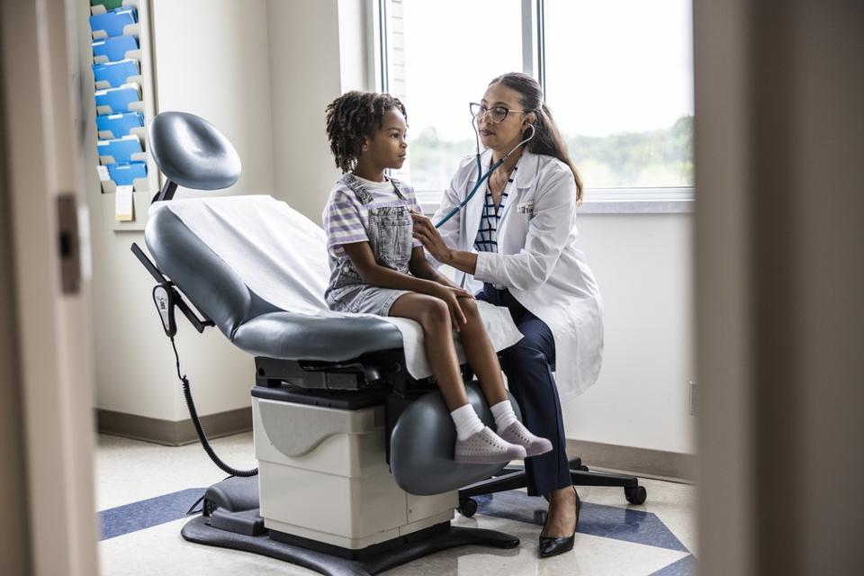 Female doctor listening to young girl's heart in exam room