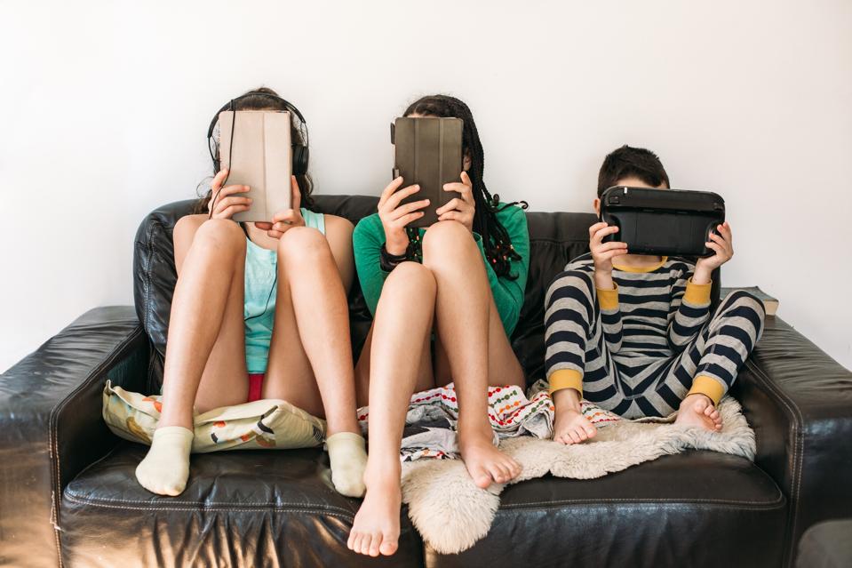 three kids with electronic devices on a sofa