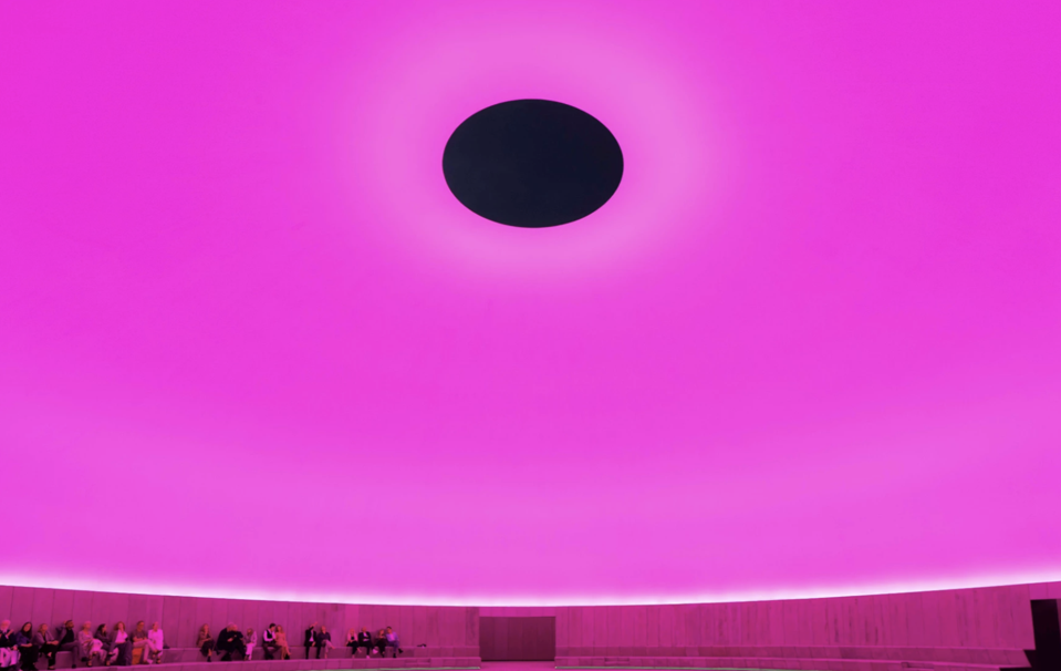 A domed hall lit pink with an ceiling aperture opening up to the black night sky