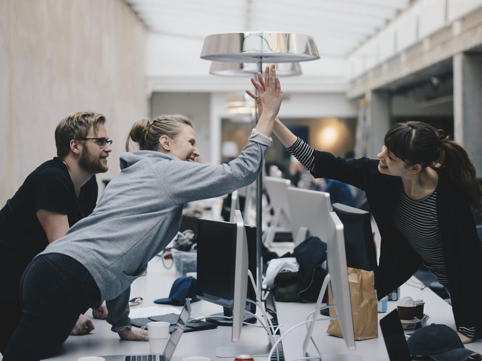 Happy female computer programmers giving high-five over desk in office