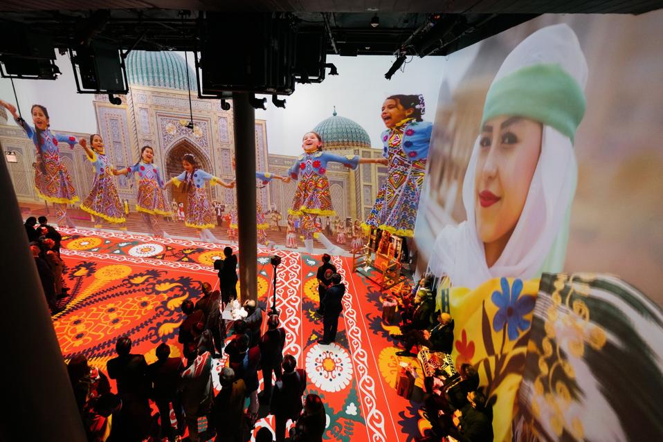 Projecrted images in a venue space of Tajik children dancing in traditional outfits.