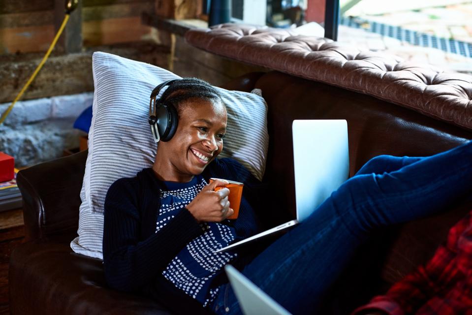 Businesswoman listening to audiobook learning AI skills, with mug, laptop & headphones