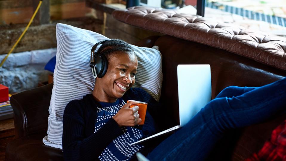 Businesswoman listening to audiobook learning AI skills, with mug, laptop & headphones