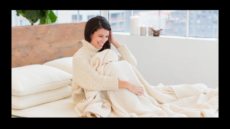Woman with brown hair and a white sweater sitting on an Avocado Green mattress.