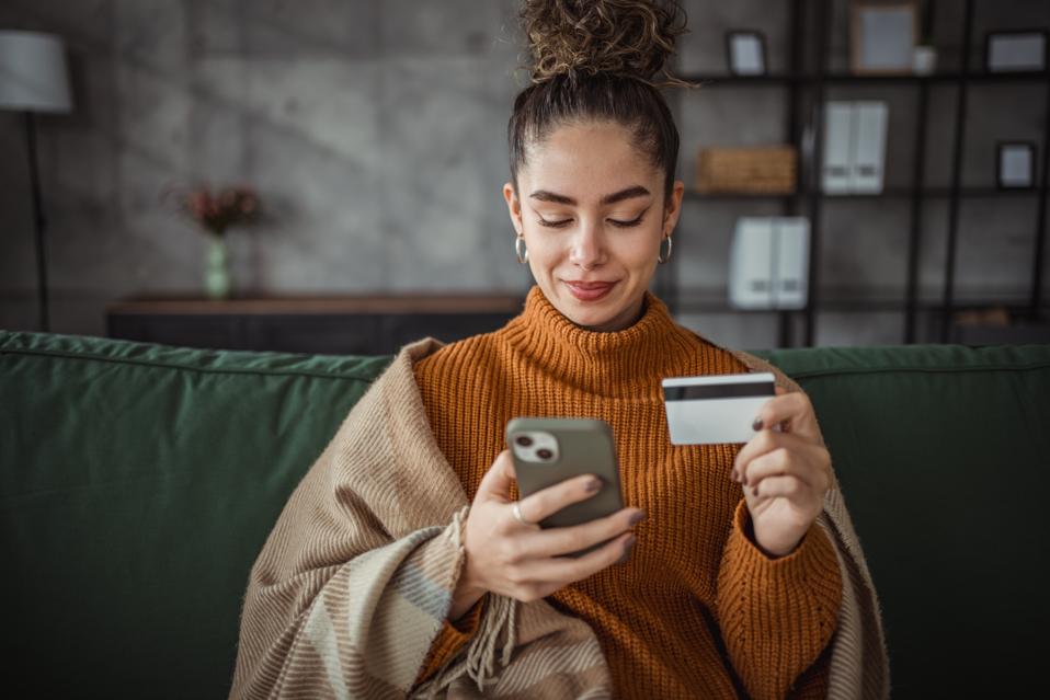 Young beautiful Caucasian woman shopping on mobile phone online using payment card