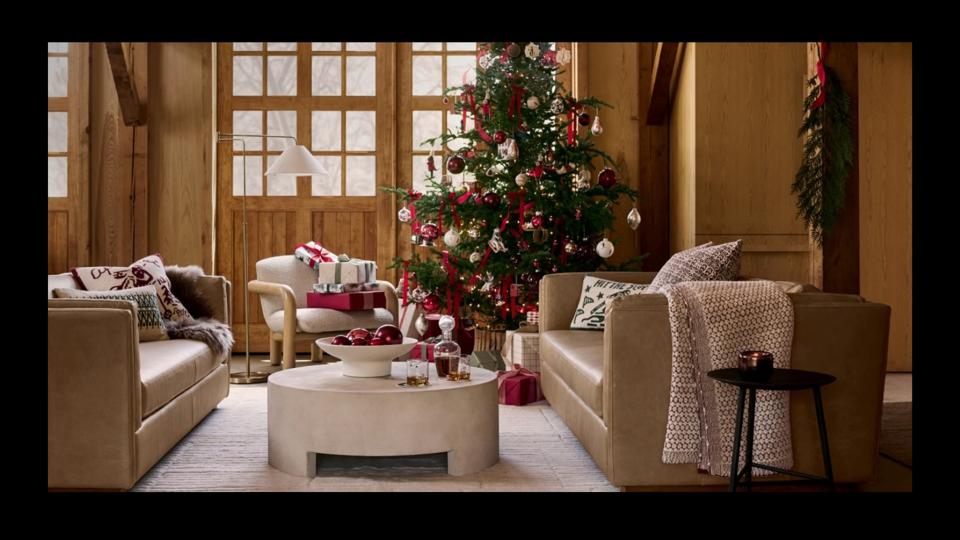 A living room with two brown couches, a decorated Christmas tree and a round stone coffee table.