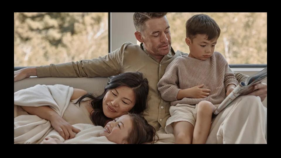 A family of four dressed in neutral clothing sitting together on a couch.