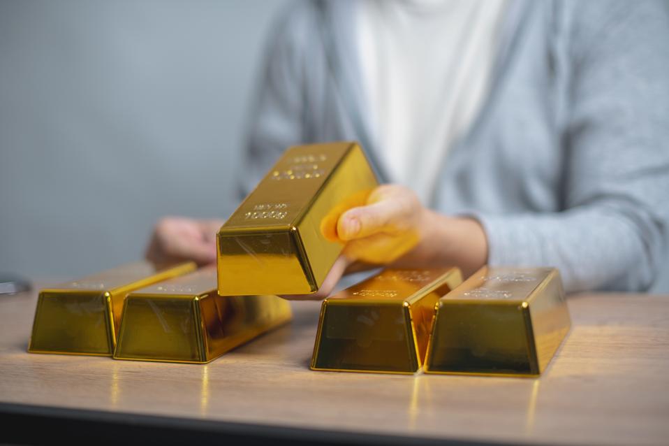 Person stacking gold bars on a table, reflecting wealth or investment in precious metals.