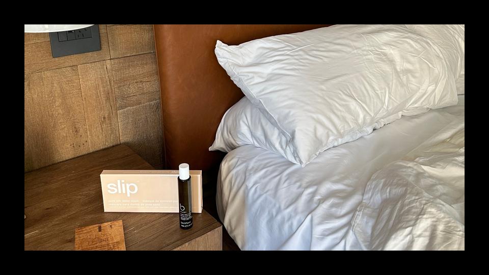 A sleep mask and pillow mist sitting on a nightstand of a hotel with a black border.