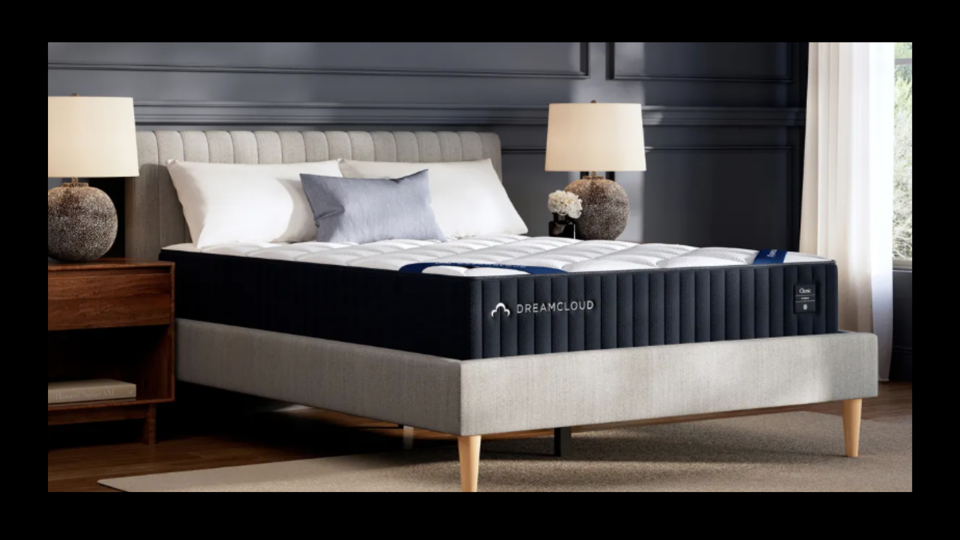 DreamCloud Classic Hybrid Mattress on gray bed frame with night stands and lamps on each side.