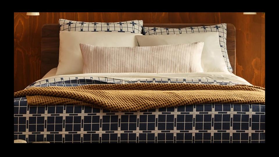 A bed with several pillows, a blue and white patterned comforter and a mustard yellow blanket.