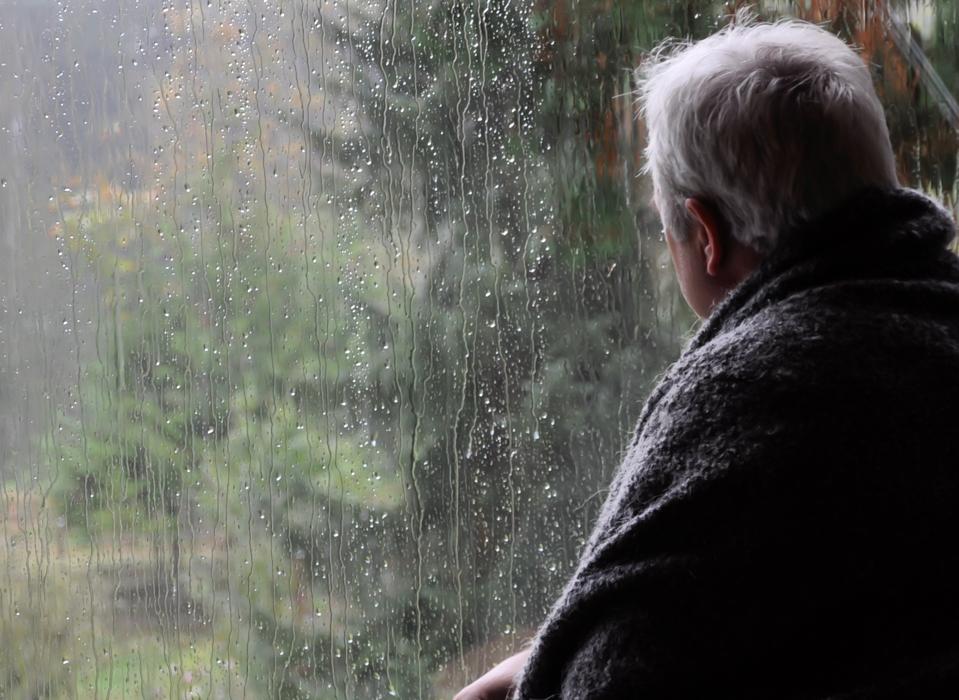Man wrapped in a blanket looking out of a window on a Rainy Day
