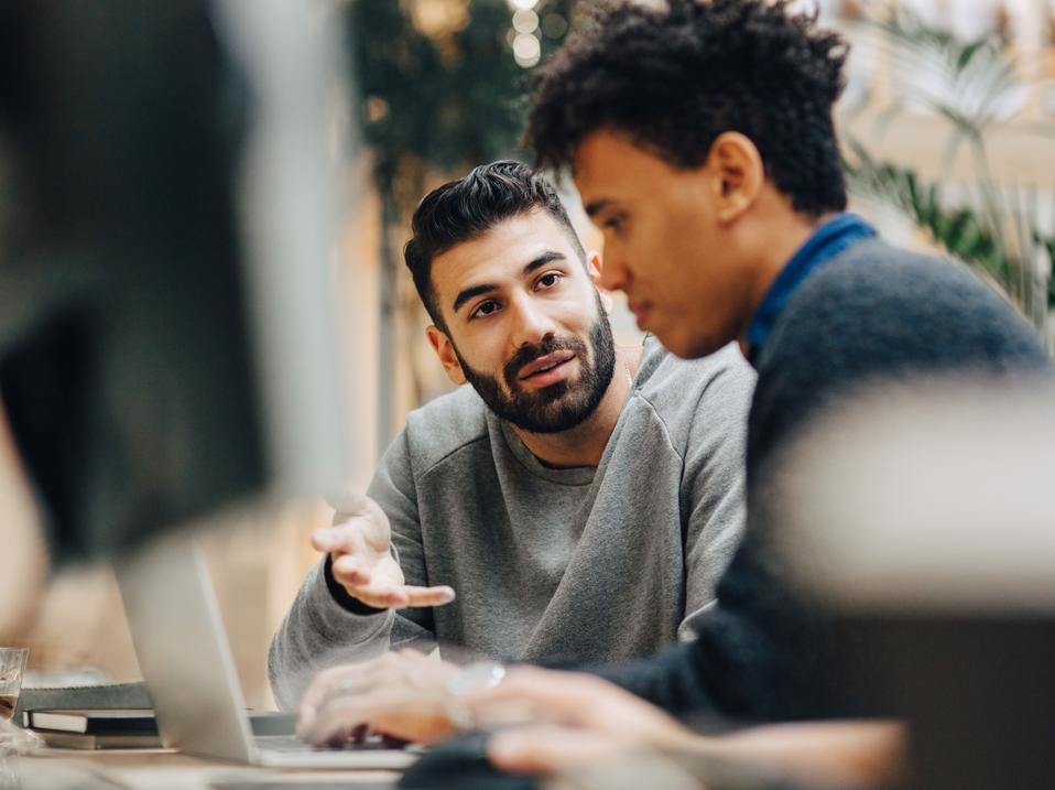 Male computer programmers discussing over laptop on desk while sitting in office