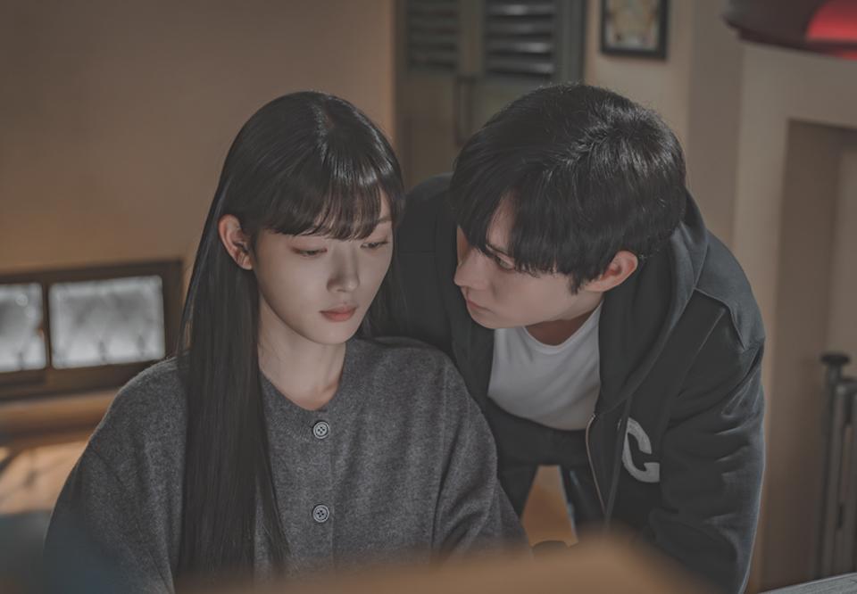 A man leans over a woman sitting at a desk.