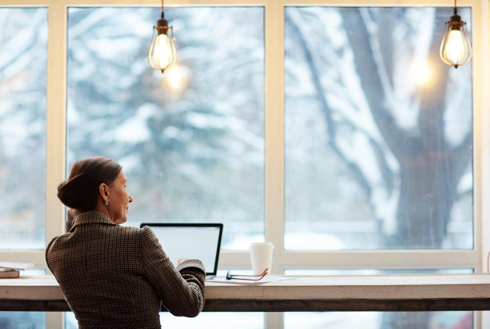 Businesswoman with laptop looking through window while spending time in cafe.