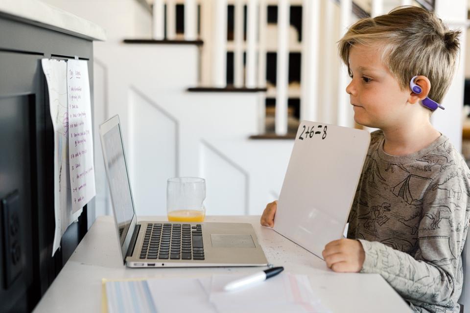 Little boy online with his classmates during video conference call, doing his work on a whiteboard and sharing his math work