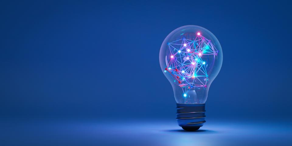 Illustration of a lightbulb set in a spotlight against a dark blue background. The lightbulb contains multiple lighted nodes connected by brightly colored lights. Innovation in technology concept.