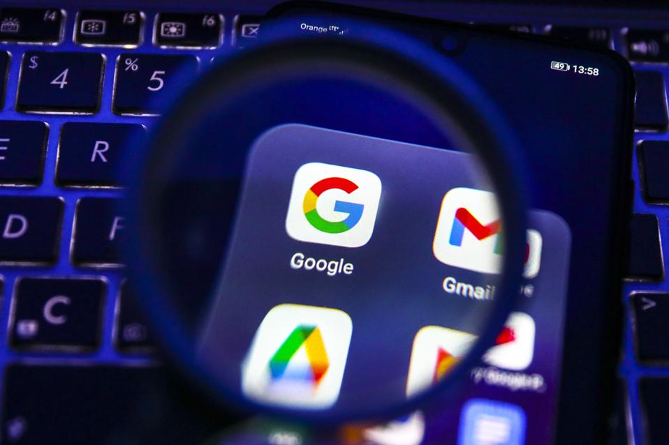 Google app is seen through a magnifying glass while being displayed on a mobile phone screen.