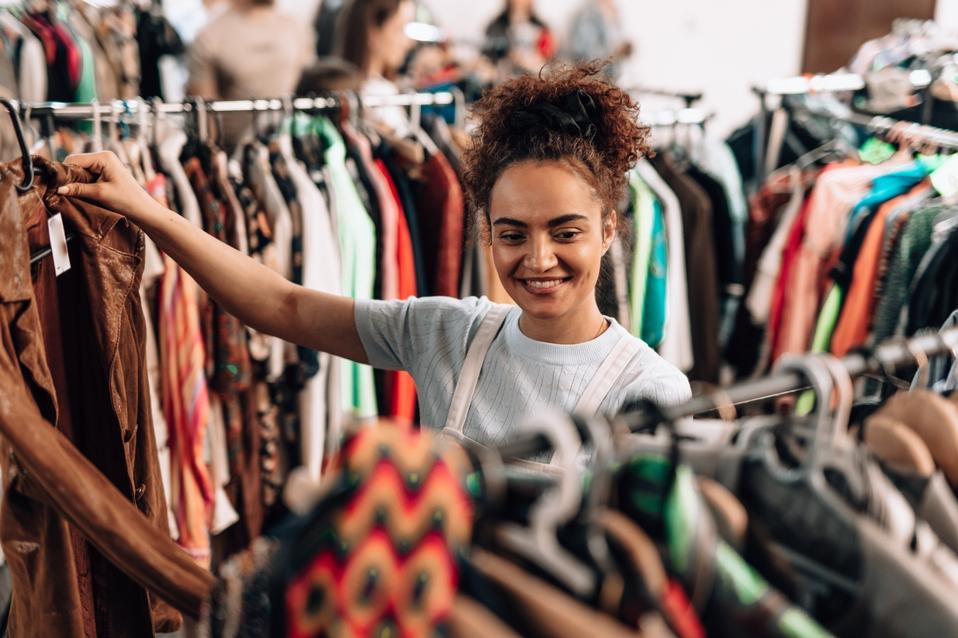 Young woman choosing clothes in a second hand shop promoting sustainable fashion