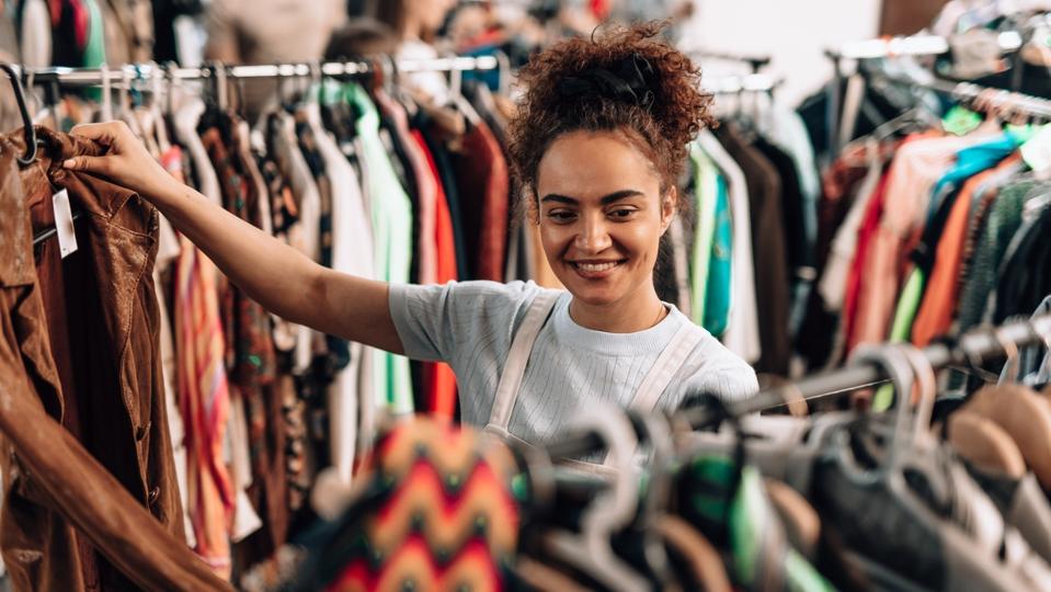 Young woman choosing clothes in a second hand shop promoting sustainable fashion