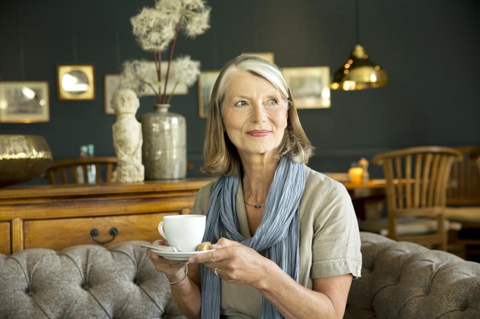 Mujer mayor sonriente en el salón con una taza de café