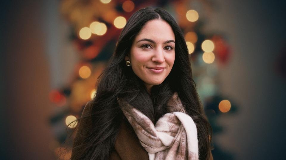 A headshot of Lucy Grace wearing a brown shirt and cream scarf