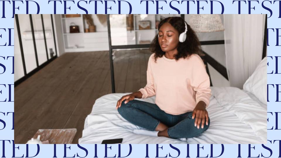 A woman meditating on a bed with her phone nearby and a blue tested border