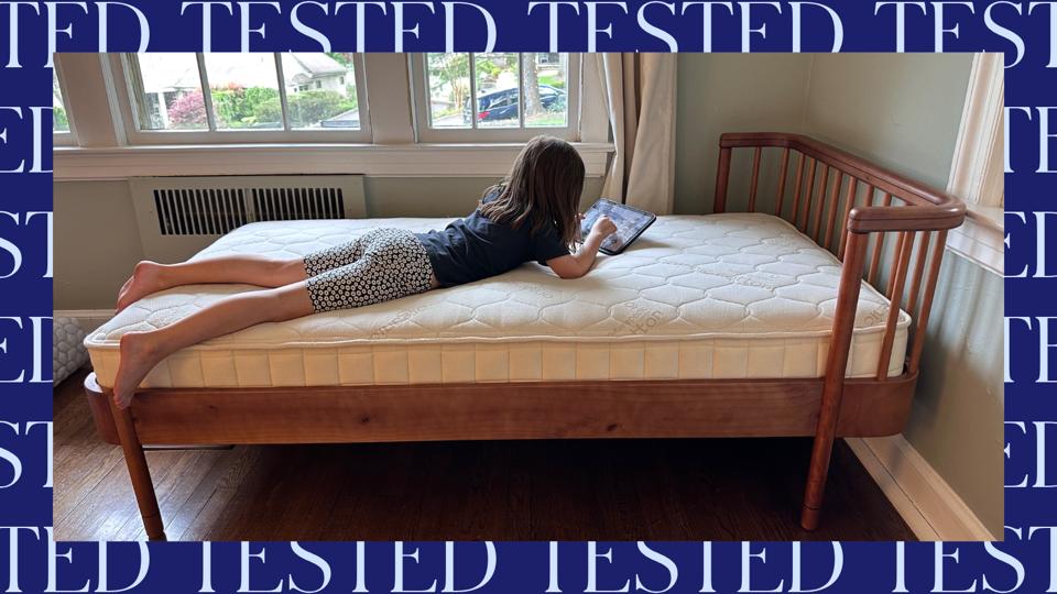A child using a tablet on top of the Naturepedic 2-In-1 Organic Kids Mattress in a bedroom