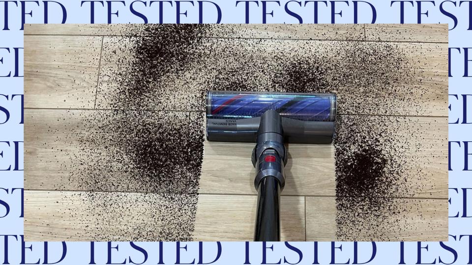 Dyson vacuum leaving a clean line through a pile of coffee grounds on wooden floor
