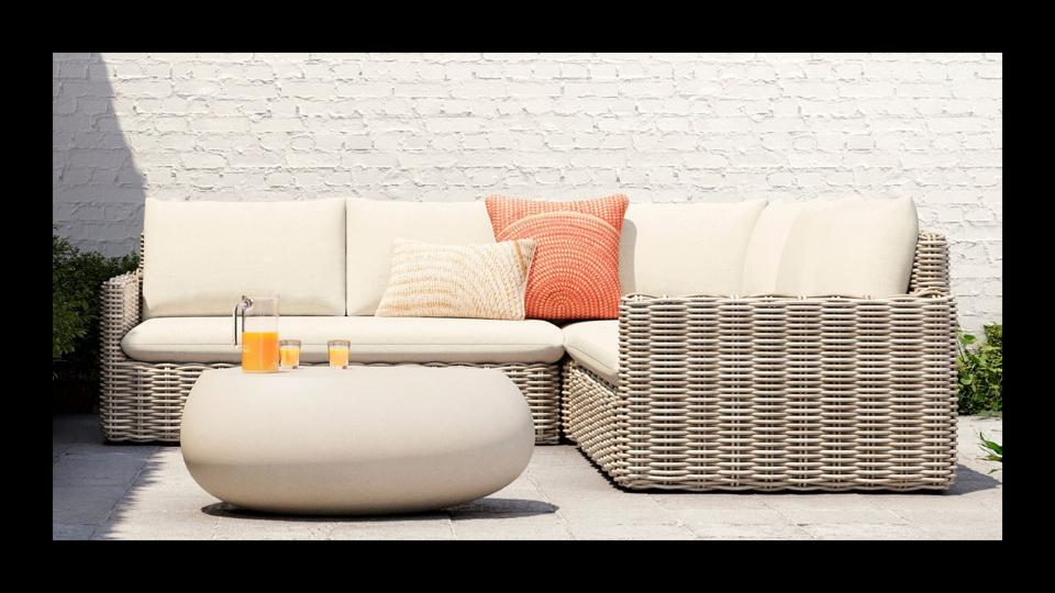 West Elm Westport Wicker Slim Profile Outdoor Sectional in front of white brick wall oudoors