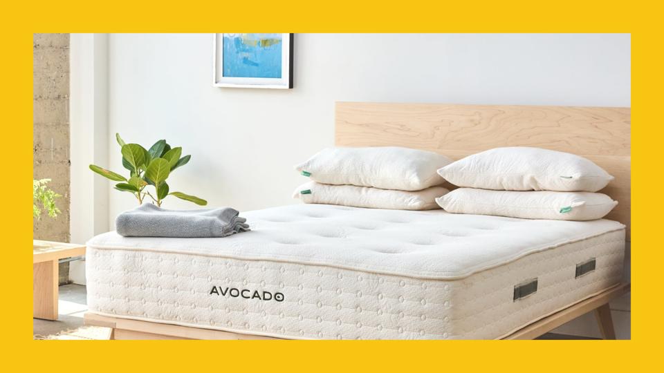 An Avocado mattress on a wooden frame bed with four pillows and a blanket on top