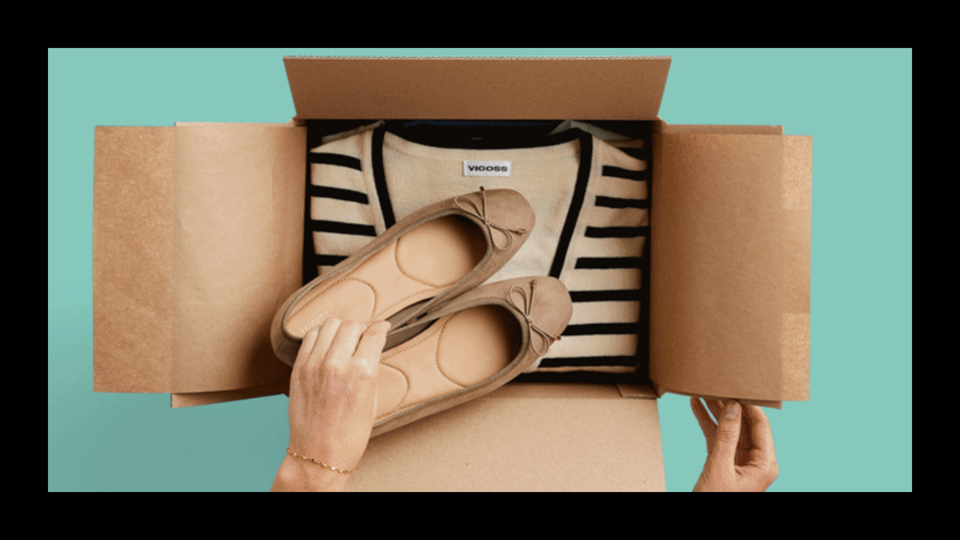 A hand reaching into a box with a sweater and a pair of shoes inside