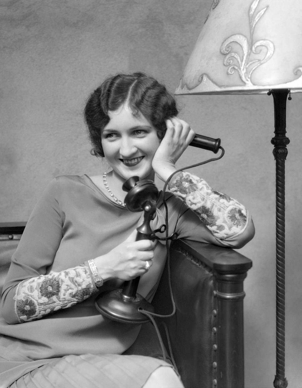 Woman On Candle Stick Phone Sitting On Couch By Lamp Smiling Flirting.
