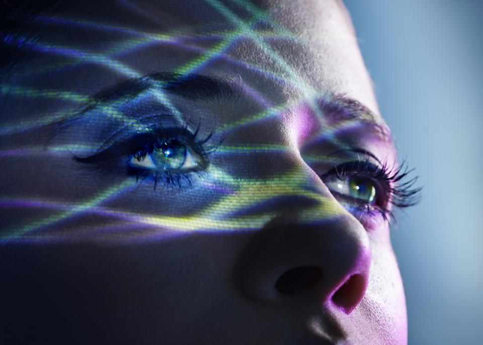 Thin light beams going across the eyes of a woman, shot against a blue studio background