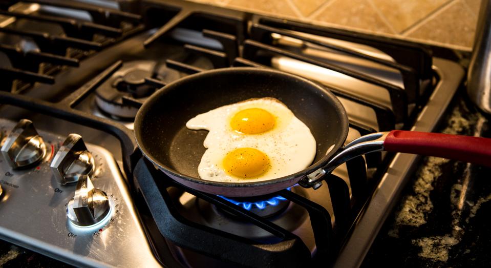 Two eggs being fried in a non-stick skillet on a gas range.