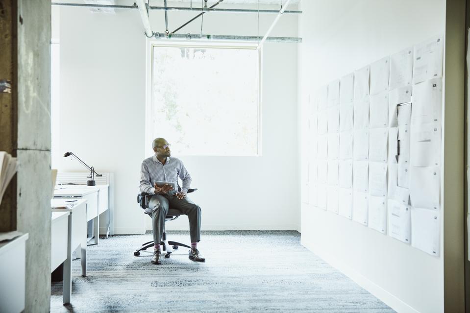 Businessman reviewing project plans on office wall while working on digital tablet