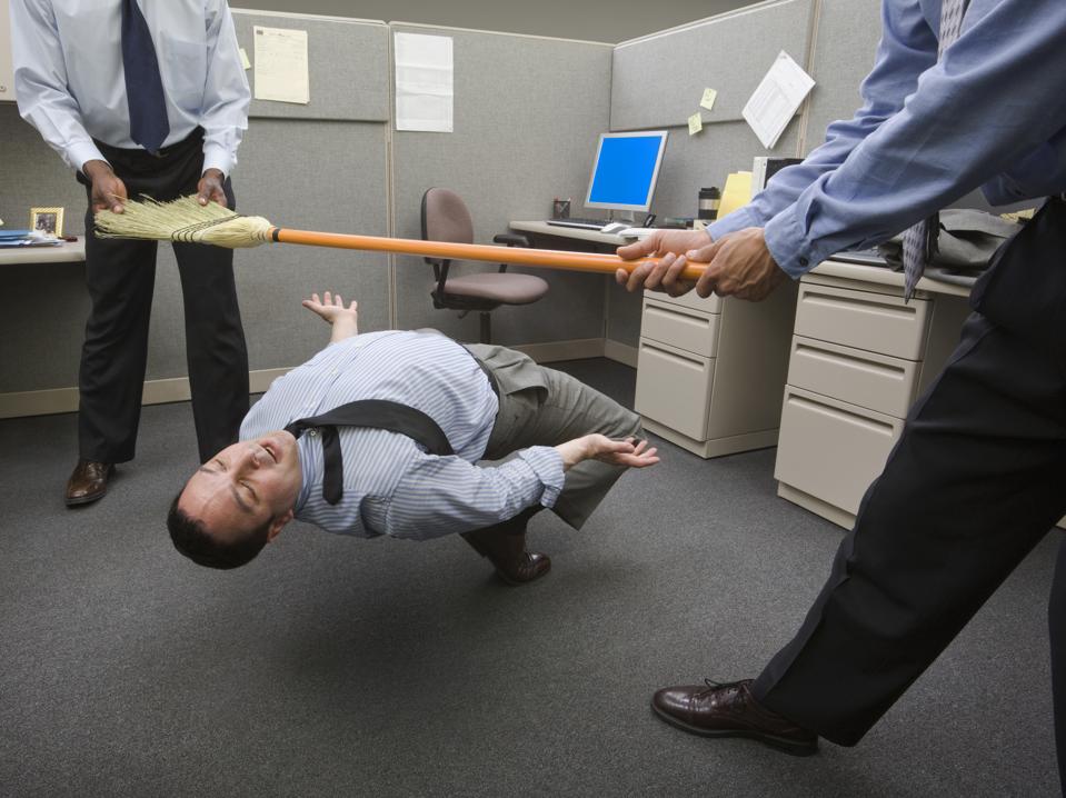 Businessmen playing limbo with broom in office