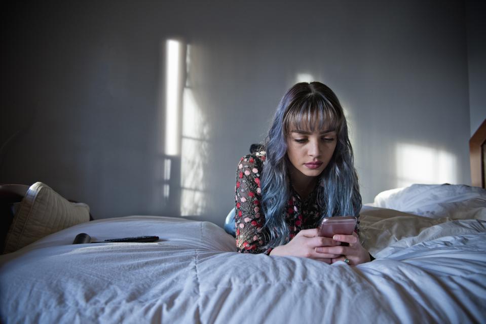 Teen with long hair looks at phone on bed