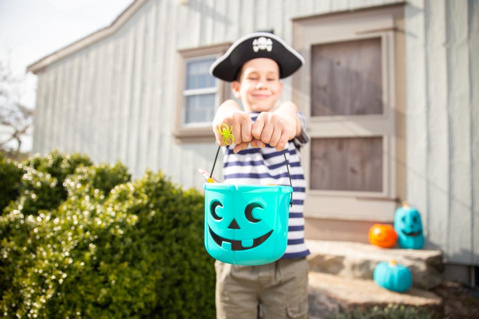 cheerful boy holding a teal bucket with toys and pencils in Halloween