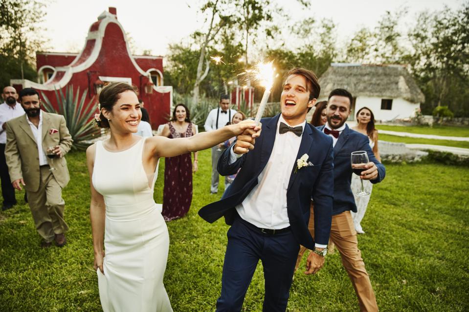 Bride and groom holding sparkler while celebrating during outdoor wedding reception with friends