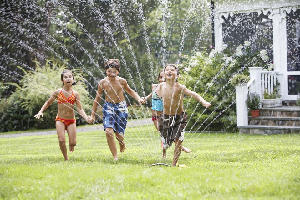 Four kids (8-10) playing in garden with sprinkler