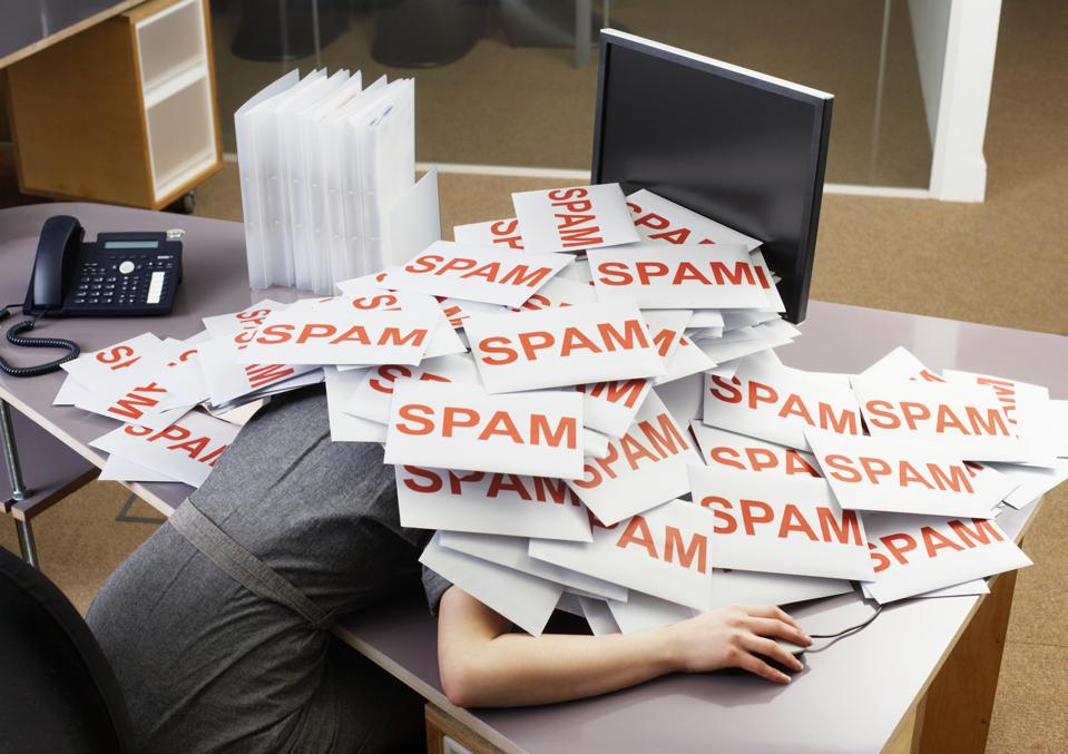 Young businesswoman at her desk covered in a pile of envelopes with SPAM on them